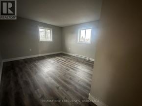 Gananoque triplex for rent - A room with wooden flooring and two windows.