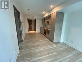 Toronto (Waterfront Communities) condo for rent - A spacious room with wooden flooring and a kitchen area in the background.