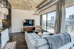 Toronto (Waterfront Communities) condo for rent - A modern living room with a grey sofa and a kitchen area with white appliances.