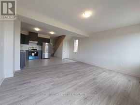 Zorra (Thamesford) townhouse for rent - A spacious room with wooden flooring and a kitchen area in the background.