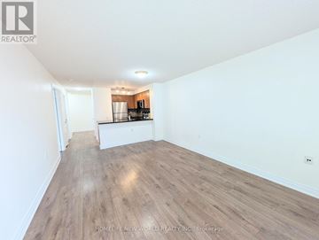 Toronto (Willowdale East) condo for rent - A spacious room with wooden flooring and a kitchen area in the background.