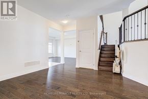 New Tecumseth (Alliston) apartment for rent - A spacious room with wooden floors and white walls, featuring a staircase with a black railing.