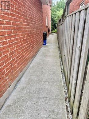 Mississauga (Hurontario) apartment for rent - A narrow sidewalk runs between a red brick wall and a wooden fence.