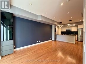 Toronto (Islington-City Centre West) condo for rent - A spacious room with wooden flooring and a kitchen area in the background.