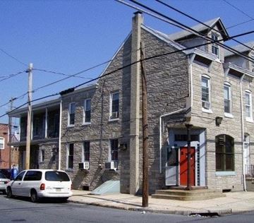 Reading apartment for rent - A grey stone building with a red door and a white car parked in front.