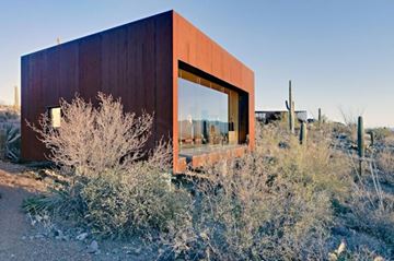 Raleigh apartment for rent - A modern house with a large window and a brown exterior is surrounded by desert vegetation.