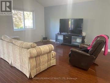Kitchener apartment for rent - A woman sits on a brown leather chair in a living room with a large couch and a television.