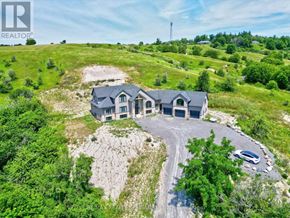 Cramahe apartment for rent - A large house with a grey roof is surrounded by greenery and a gravel driveway.
