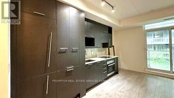 Toronto (Waterfront Communities) condo for rent - A kitchen with dark wood cabinets and a window overlooking a green area.