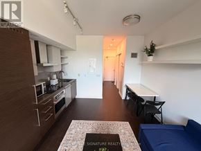 Toronto (Niagara) condo for rent - A living room with a blue couch and a kitchen area with a stove and chairs.