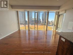 Mississauga (City Centre) condo for rent - A room with wooden flooring and a view of a city skyline through large windows.