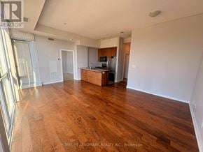 Mississauga (City Centre) condo for rent - A spacious living room with wooden flooring and a kitchen area in the background.