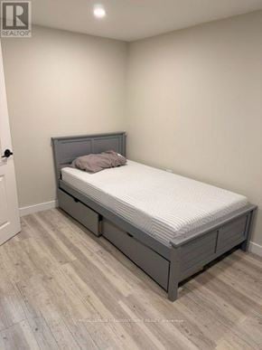 Vaughan (West Woodbridge) house for rent - A bed with a grey headboard and footboard is in a room with light grey walls and light wooden flooring.