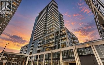 Milton (Tm Timberlea) house for rent - A tall building with a glass facade stands in the foreground with a sunset sky in the background.