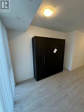 Toronto (Waterfront Communities) condo for rent - A black wardrobe stands in a room with a wooden floor.