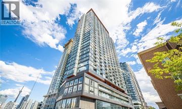Toronto condo for rent - A tall building with a glass facade stands in front of a partly cloudy sky.