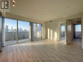 Toronto (Waterfront Communities) condo for rent - A spacious room with wooden flooring and large windows overlooking a city skyline.