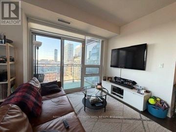 Toronto (Moss Park) condo for rent - A living room with a brown leather couch and a flat screen TV mounted on the wall.