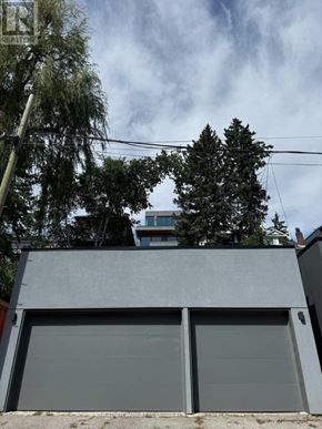 Toronto (North Riverdale) apartment for rent - A grey garage door is closed and there is a tree in front of a building.