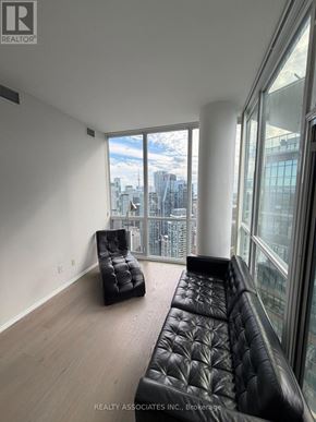 Toronto (Church-Yonge Corridor) condo for rent - A black leather sofa sits in a room with a view of the city.