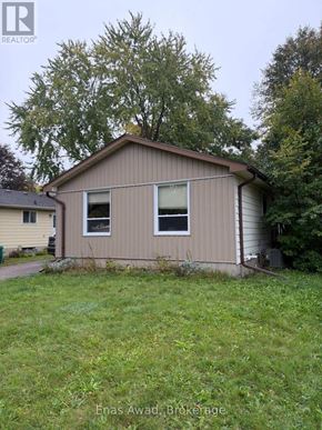 Waterloo apartment for rent - A small house with a brown roof and a beige siding is surrounded by green grass and trees.