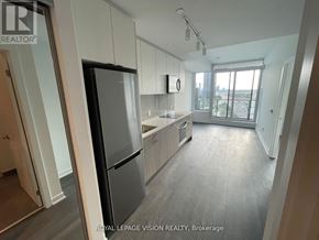 Toronto (South Parkdale) condo for rent - A kitchen with a refrigerator, cabinets, and a window overlooking a parking lot.