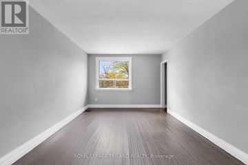 London East (East K) multi-family for rent - A spacious room with wooden flooring and a window showing a tree outside.