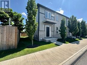 St. Catharines (Oakdale) townhouse for rent - A modern house with a grey facade and a white door is surrounded by greenery.