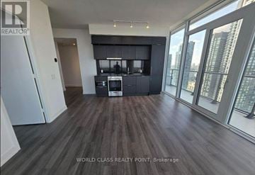 Mississauga (City Centre) condo for rent - A spacious living room with wooden flooring and a kitchen area in the background.