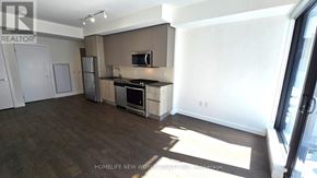 Toronto (Waterfront Communities) condo for rent - A spacious room with wooden floors and white walls, with a kitchen area visible on the right.