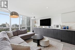 Toronto (Waterfront Communities) condo for rent - A modern living room with a large grey sofa and a flat screen TV mounted on the wall.