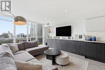 Toronto (Waterfront Communities) condo for rent - A modern living room with a large grey sofa and a flat screen TV mounted on the wall.