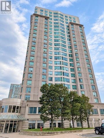 Toronto (Woburn) condo for rent - A tall building with a glass facade stands under a blue sky.