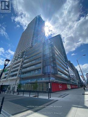 Toronto (Newtonbrook East) condo for rent - A tall building with a glass facade stands in front of a blue sky with clouds.