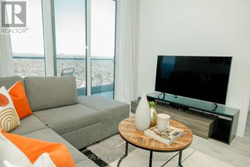 Toronto (Newtonbrook East) condo for rent - A living room with a grey couch, a round wooden table with a vase and a book on it, and a flat screen TV mounted on the wall.