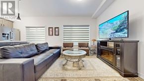 Niagara Falls (Hospital) townhouse for rent - A living room with a black leather couch, a round glass table, and a flat screen TV mounted on the wall.