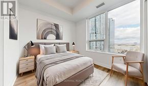 Vaughan (Vaughan Corporate Centre) condo for rent - A bedroom with a large bed, a chair, and a window overlooking a cityscape.
