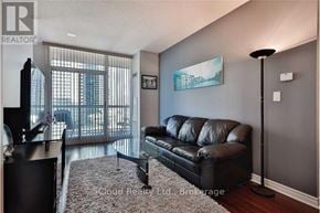 Mississauga (Hurontario) condo for rent - A black leather sofa sits in a living room with a large window and a painting on the wall.