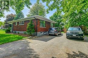 Ottawa apartment for rent - A house with a red brick exterior is surrounded by greenery and has two vehicles parked in front.