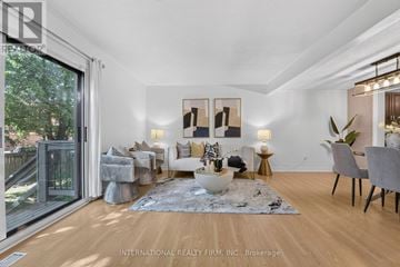 Mississauga (Meadowvale) townhouse for rent - A well-lit, spacious living room with a grey rug, a grey sofa, a white armchair, a grey chair, a wooden floor, a glass door, a table with a vase, a potted plant,