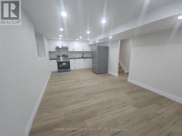 Brantford apartment for rent - A spacious room with wooden flooring and white walls, featuring a kitchenette with a refrigerator, oven, and cabinets.