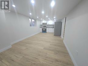 Brantford apartment for rent - A spacious room with wooden flooring and a kitchenette in the background.