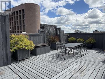 Ottawa condo for rent - A wooden deck with a table and chairs in the foreground and a building in the background.