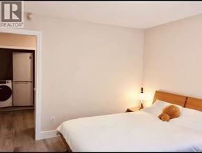Vancouver apartment for rent - A bedroom with a bed, a lamp, and a door leading to a laundry room.