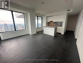 Mississauga (City Centre) condo for rent - A spacious room with wooden flooring and large windows overlooking a cityscape.