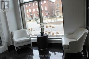 Markham (Wismer) condo for rent - Two white chairs are placed in front of a window with a view of a street and buildings.