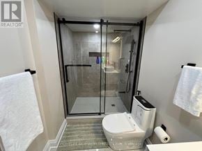Oshawa (Taunton) apartment for rent - A white toilet is in a bathroom with a walk-in shower.