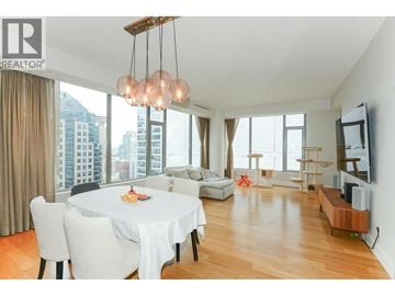 Vancouver apartment for rent - A well-lit, spacious living room with a dining table and chairs, a television, and a large window with a view of the city.