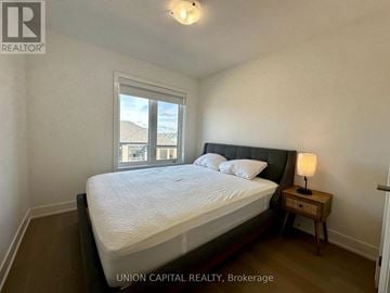 Markham (Wismer) townhouse for rent - A bedroom with a large bed, a nightstand with a lamp, and a window with a view of the beach.