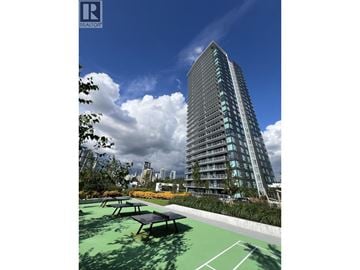Coquitlam apartment for rent - A modern building with a glass facade stands tall in a sunny park.